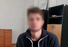 Blurry man in a dark zip-up jacket sits in an office with a wooden floor and cabinets behind him; National Police of Ukraine watermark in the corner.