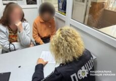 Two children sit across from a Ukrainian police officer at a table, an interview-style setting with documents on the table.