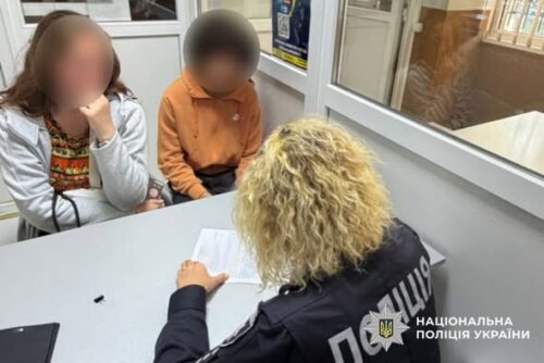 Two children sit across from a Ukrainian police officer at a table, an interview-style setting with documents on the table.