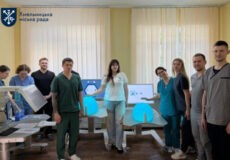 Group of people in a bright room with 3D printers and blue models on desks, posing for a team photo at Хмельницька міська рада project.