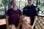 Ukrainian policewoman in uniform posing outdoors with two women and two young girls, all standing beside a decorative metal fence; some faces pixelated for privacy.
