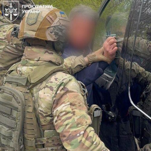 Camouflage-clad soldier restrains a man at a car window during an arrest; watermark of the Ukrainian Prosecutor's Office in the corner.