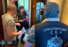 SBU special forces officer in blue jacket questions two blurred suspects in a doorway hallway during a raid.