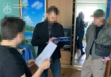 Three men indoors, one holds papers and a blue folder/tablet; Ukrainian Prosecutor's Office logo in the top-left, faces blurred.
