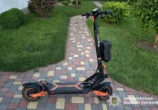 Electric scooter with orange accents parked on a brick-paver path in a grassy front yard.