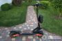 Electric scooter with orange accents parked on a brick-paver path in a grassy front yard.