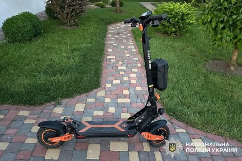 Electric scooter with orange accents parked on a brick-paver path in a grassy front yard.