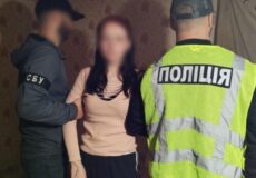 Two police officers detain a woman indoors; one wears a neon vest marked 'ПОЛІЦІЯ' and stands beside them.