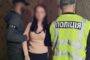 Two police officers detain a woman indoors; one wears a neon vest marked 'ПОЛІЦІЯ' and stands beside them.