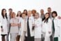 Group of doctors and nurses in white coats posing together as a healthcare team, smiling at the camera.