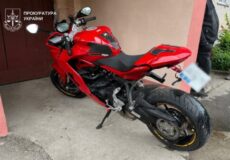 Red sport motorcycle parked by a pink wall, with a blurred license plate; Ukrainian Prosecutor's Office watermark in the top left.
