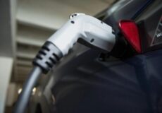Close-up of a charging plug inserted into an electric car's charging port in a garage or station setting.