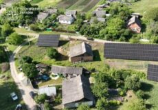 Aerial view of a rural Ukrainian village with wooden houses and large solar panels on rooftops and in nearby fields.