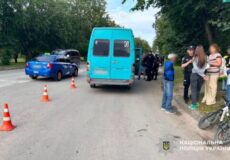 Blue minibus stopped on a road with orange traffic cones, police officers and bystanders nearby; Ukrainian police logo in corner.
