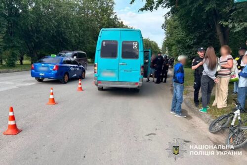 Blue minibus stopped on a road with orange traffic cones, police officers and bystanders nearby; Ukrainian police logo in corner.