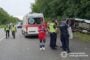 Emergency responders, an ambulance, and police at a highway crash; a vehicle lies on its side by a grassy verge behind them.