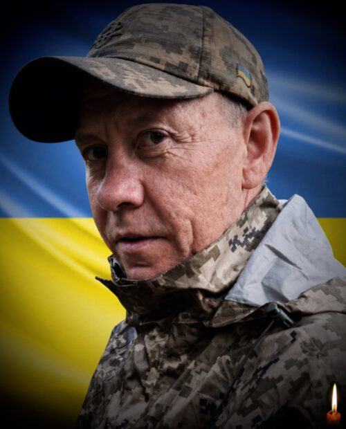 Close-up of a soldier in camouflage with the Ukrainian flag behind him.