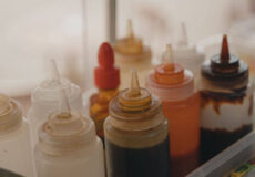 Assorted squeeze bottles with white, yellow, red, and brown sauces in a kitchen prep area. (informative)