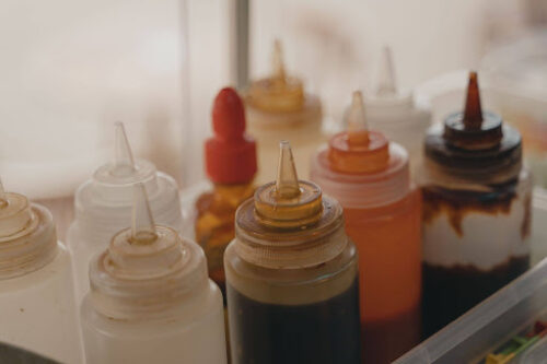 Assorted squeeze bottles with white, yellow, red, and brown sauces in a kitchen prep area. (informative)