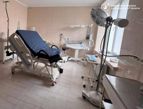 Empty hospital room with an adjustable blue bed on wheels, IV stand, and medical equipment nearby.