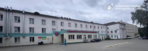 Wide view of a public medical facility with a pale building, teal entrance awning, and parked cars outside; Ombudsman of Ukraine watermark in the top-right corner.