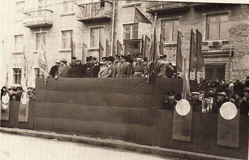 Black-and-white photo of a parade float with people and flags on a city street.