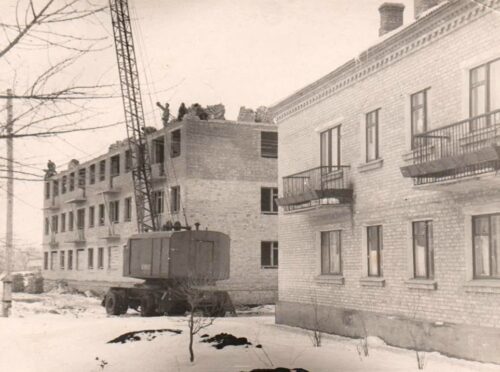 Construction site with workers on top of an unfinished brick building, a crane, and a truck in a snowy yard.