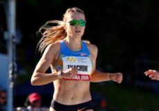 Female runner wearing a blue top and green sunglasses sprinting in a race, bib visible on her chest.
