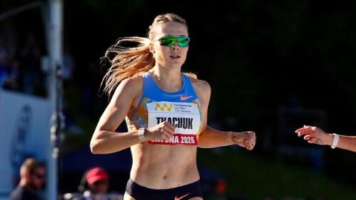 Female runner wearing a blue top and green sunglasses sprinting in a race, bib visible on her chest.