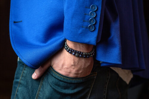 Close-up of a person wearing a cobalt blue blazer with a beaded bracelet, hand in a jeans pocket.