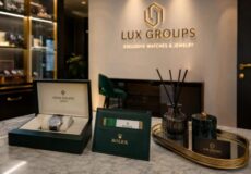 Lux Groups showroom display with an open Rolex watch box, green Rolex presentation box, and a diffuser on a marble counter near the store logo in the background.