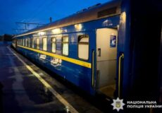 Blue passenger train car at a wet platform at dusk, door open on the side.