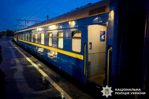 Blue passenger train car at a wet platform at dusk, door open on the side.