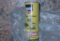 Yellow spray can with a Cyrillic label partially wrapped in a clear plastic bag on a speckled countertop.