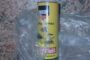 Yellow spray can with a Cyrillic label partially wrapped in a clear plastic bag on a speckled countertop.