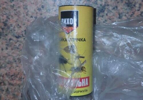 Yellow spray can with a Cyrillic label partially wrapped in a clear plastic bag on a speckled countertop.