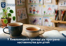 Banner showing two mugs on a wooden table with kids' drawings on the wall and the Khmelnytskyi City Council logo, promoting a children's mentoring program.