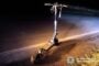 Nighttime scene of a damaged electric scooter on the roadside, police badge visible in the lower-right corner.