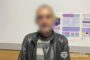 Blurry man in a black leather jacket and striped sweater standing indoors beside informational posters, with National Police of Ukraine logo.