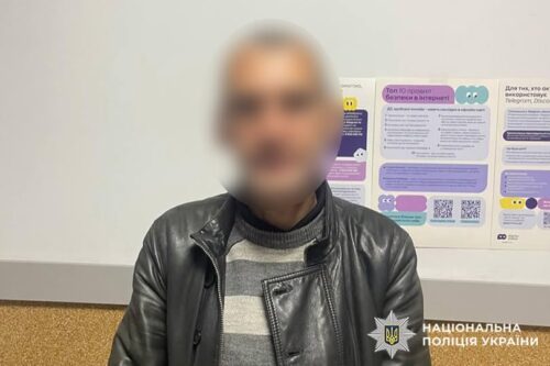 Blurry man in a black leather jacket and striped sweater standing indoors beside informational posters, with National Police of Ukraine logo.