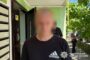 Man in a black Adidas shirt stands outside a building by a row of mailboxes; face blurred.