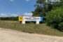 Billboard on a grassy roadside with blue and yellow panels reading 'Будинок - Інтернат' and a logo, set near trees and a dirt road.