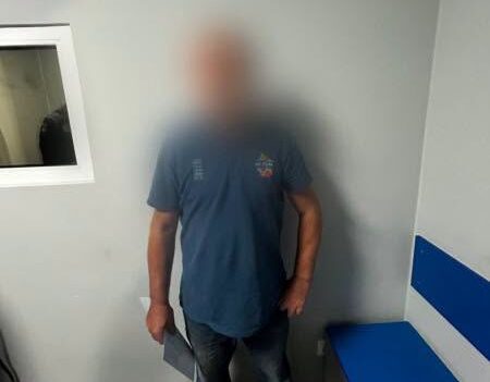 Blurry photo of a man in a blue T-shirt standing in a small room with pale walls and blue benches; Ukrainian police watermark in the bottom right.
