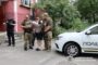 Ukrainian police officers arrest a man beside a white patrol car while a bystander and another guard observe nearby.