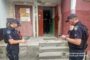 Two Ukrainian police officers in dark uniforms and caps stand on concrete steps outside a building, looking at tablet devices.