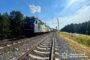 Electric locomotive hauling a long train along a rural tracks scene with overhead wires and a blue sky; Ukrainian police watermark visible.