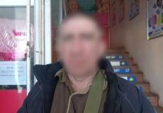 Blurred man in a dark jacket with a green shoulder bag stands at the doorway to a building; stairs and posters visible inside. Ukrainian Police watermark.