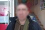 Blurred man in a dark jacket with a green shoulder bag stands at the doorway to a building; stairs and posters visible inside. Ukrainian Police watermark.