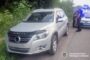 Silver SUV on a rural road with bushes; two police officers stand nearby, Ukrainian National Police emblem in the bottom-right.