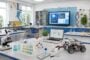 Bright science classroom lab benches with microscopes, glassware, a laptop, and a small robot on the front table.